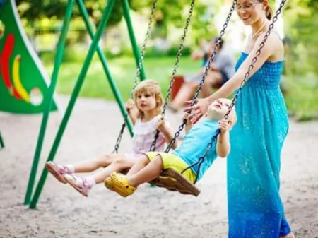 Woman pushing 2 children on a swingset